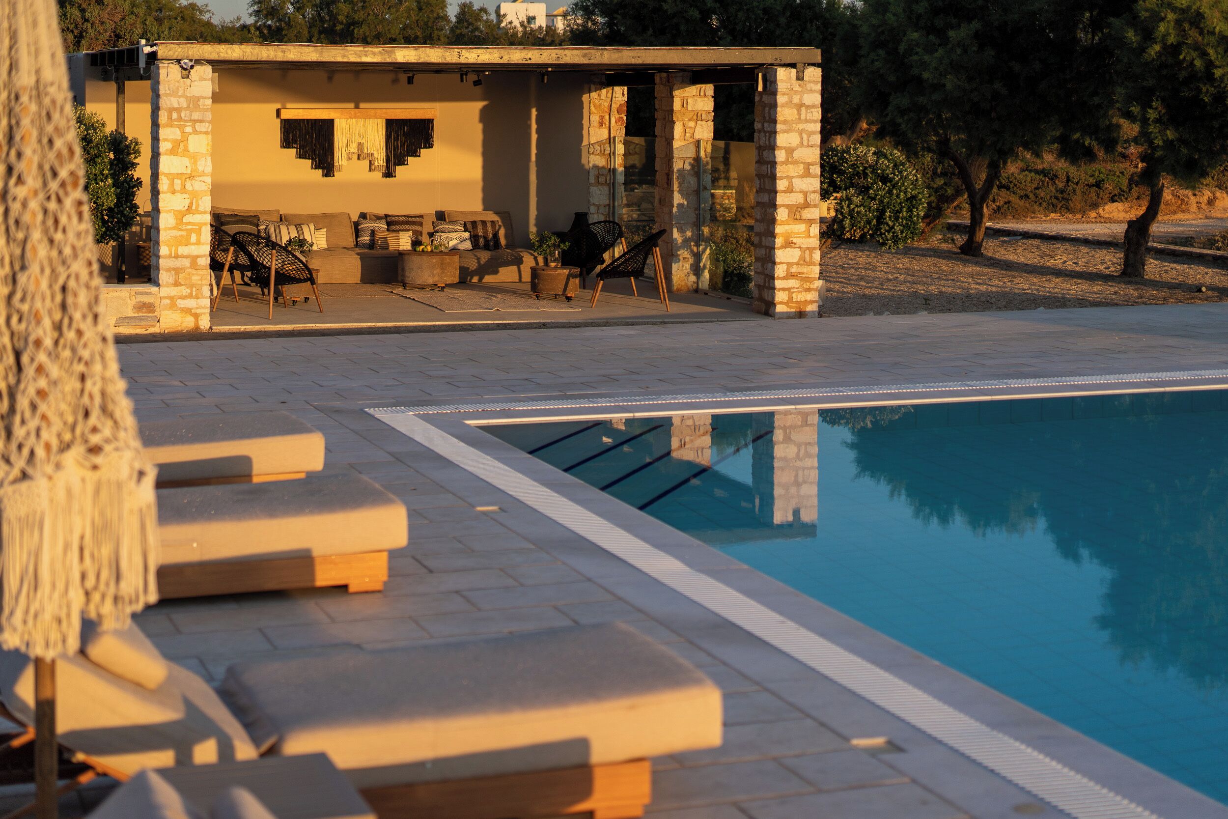 A poolside area with lounge chairs, a covered seating area, and a stone building.