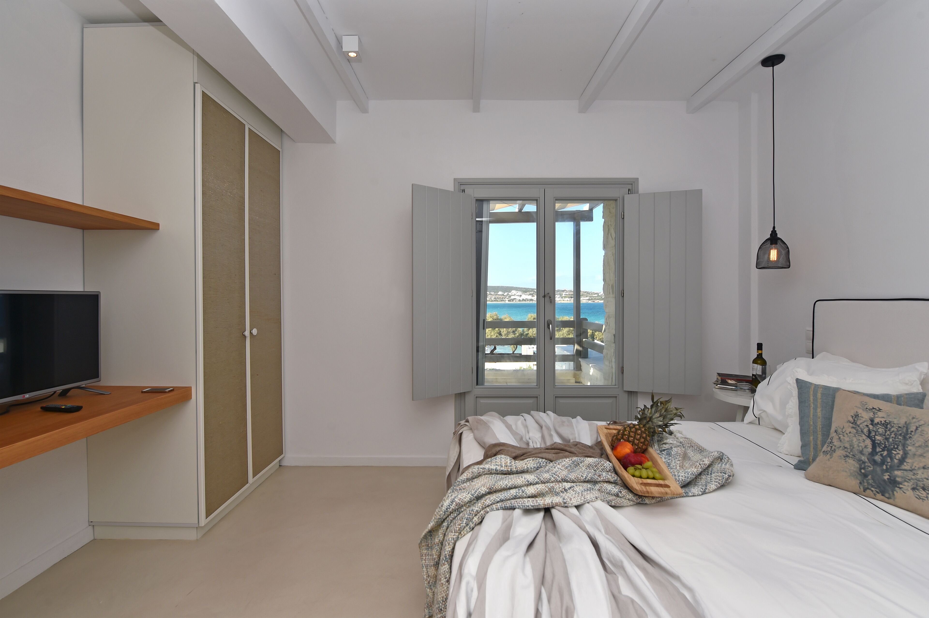 A bedroom with a bed, a TV, a window with a view, and a small table with a bottle.
