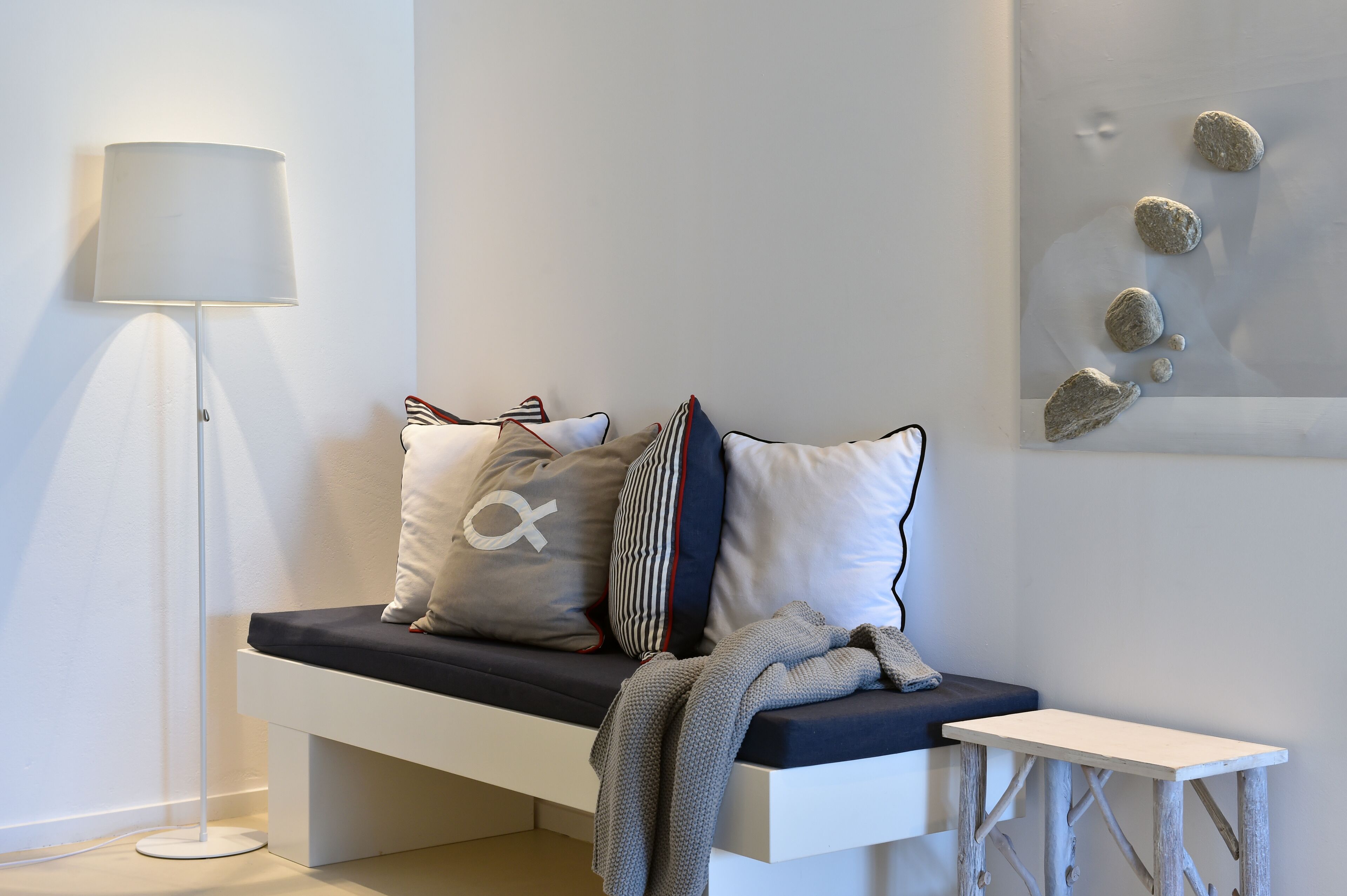A modern, minimalist room with a white bench, a floor lamp, and a wall art piece.