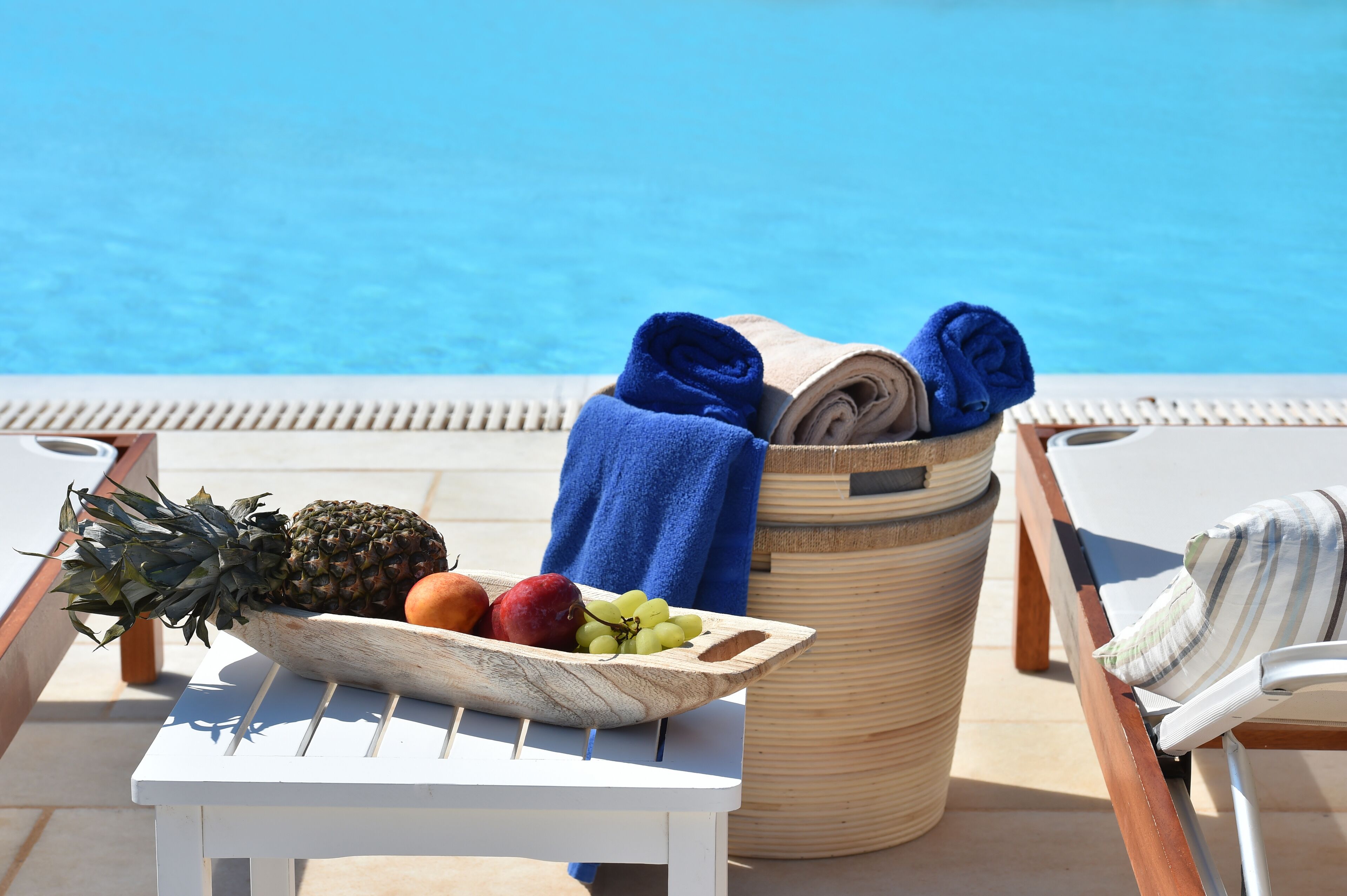 A poolside setting with a fruit bowl, towels, and lounge chairs.