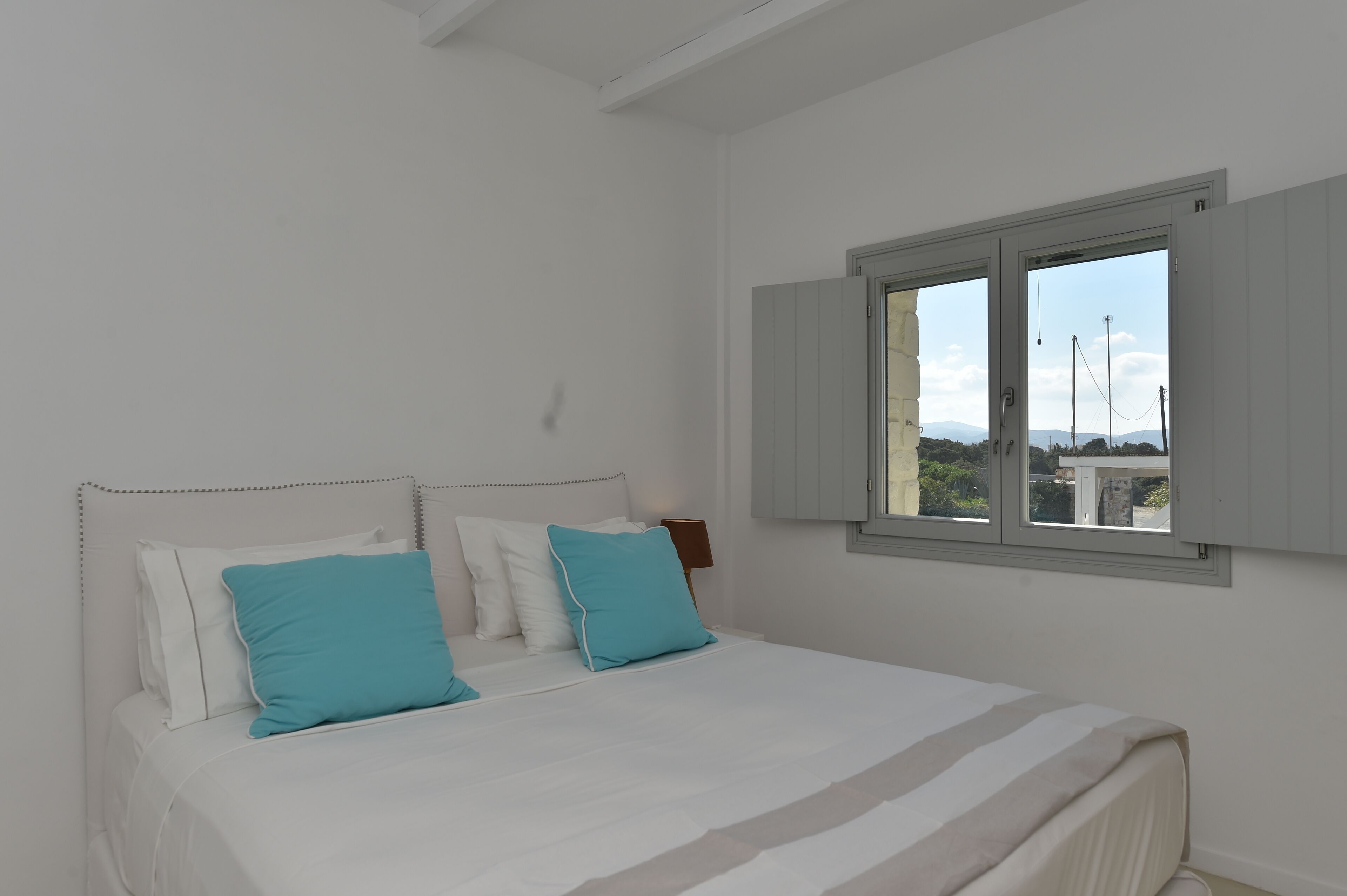 A bedroom with a large bed, white walls, and a window with shutters.