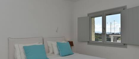 A bedroom with a large bed, white walls, and a window with shutters.