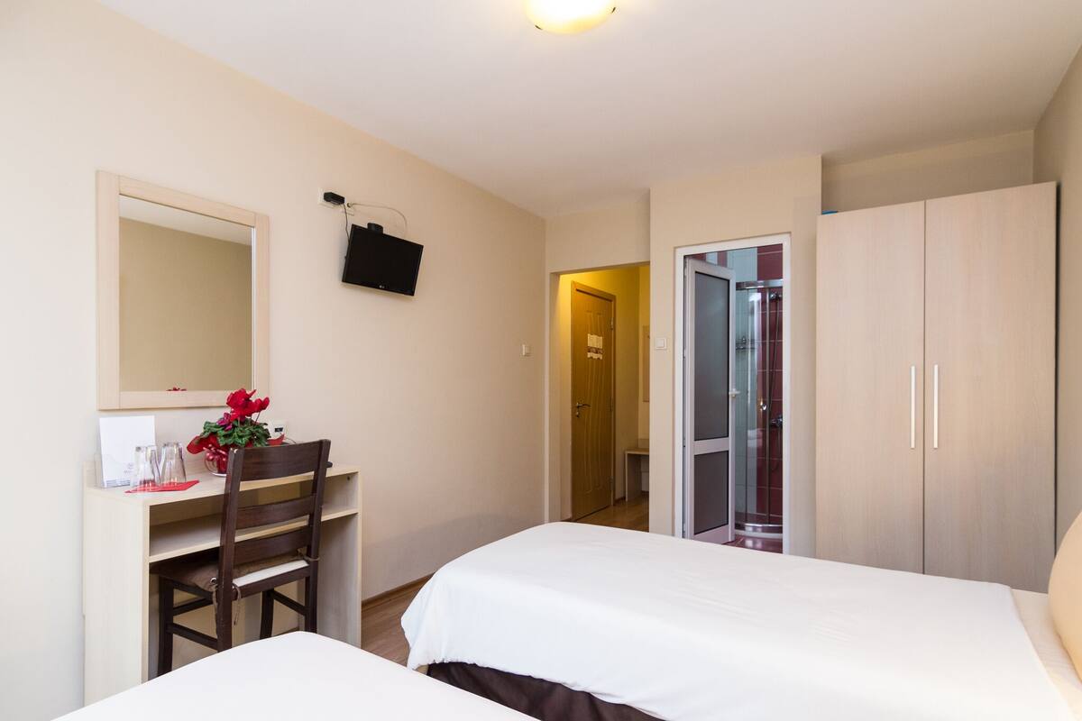 Una habitación de hotel con dos camas, un escritorio con silla, televisión y armario.