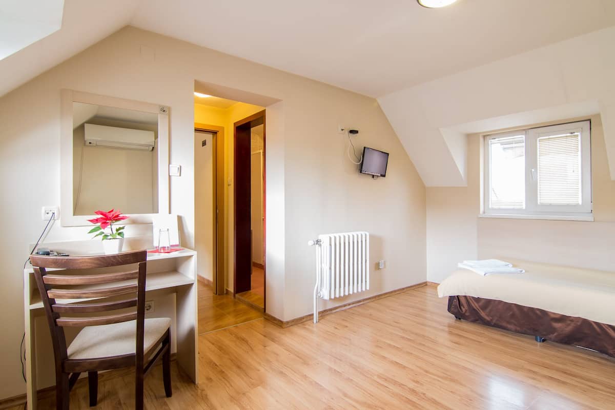 Una habitación pequeña y bien iluminada, con un escritorio de madera, una silla, una cama, un radiador y un televisor montado en la pared.