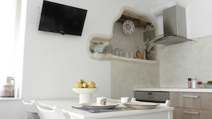 A kitchen with a white table, chairs, a bowl of fruit, a clock, and a microwave. - Nikoletta's Nest / House with large veranda  (4kms from Agia Anna,Plaka+Chora) (Naxos)