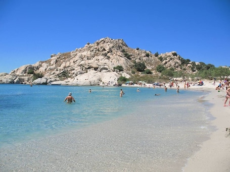 A beach with clear water, rocky hills, and people swimming and sunbathing.
