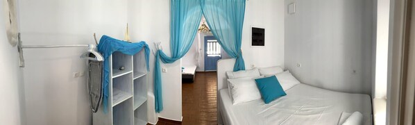 A narrow hotel room with a bed, a shelf, and a curtain.
