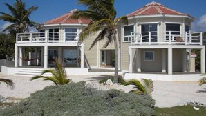 Una casa de dos pisos con un balcón, rodeada de follaje tropical.