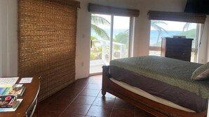 Un dormitorio con cama, cómoda de madera, televisión y vista al océano.