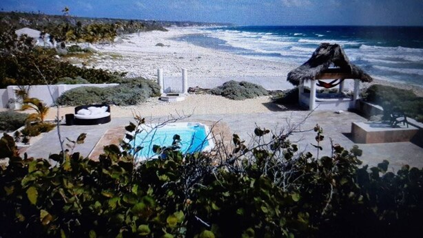 Vista de la playa con piscina, una estructura de techo de paja y vista al océano.
