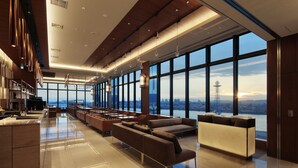 Un moderno vestíbulo de hotel con un amplio espacio de asientos, una recepción y vistas de la ciudad a través de grandes ventanales.