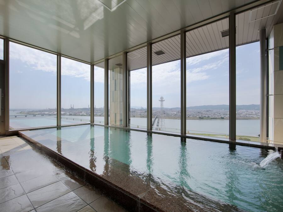 A modern indoor swimming pool with large windows offering a view of a cityscape and a body of water.