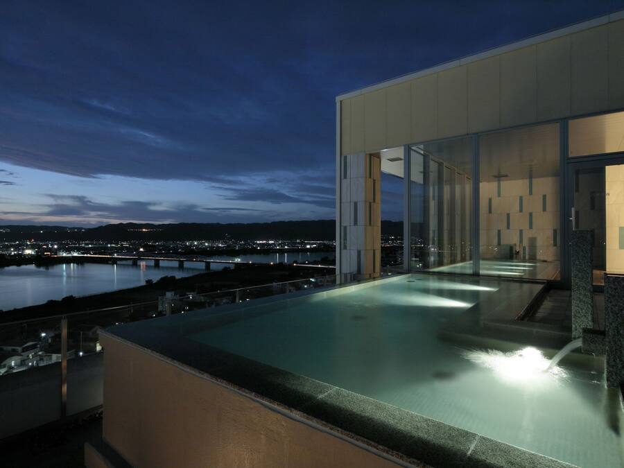 Una piscina infinita en la azotea con vistas a la ciudad, arquitectura moderna y una zona con cerramiento de cristal.
