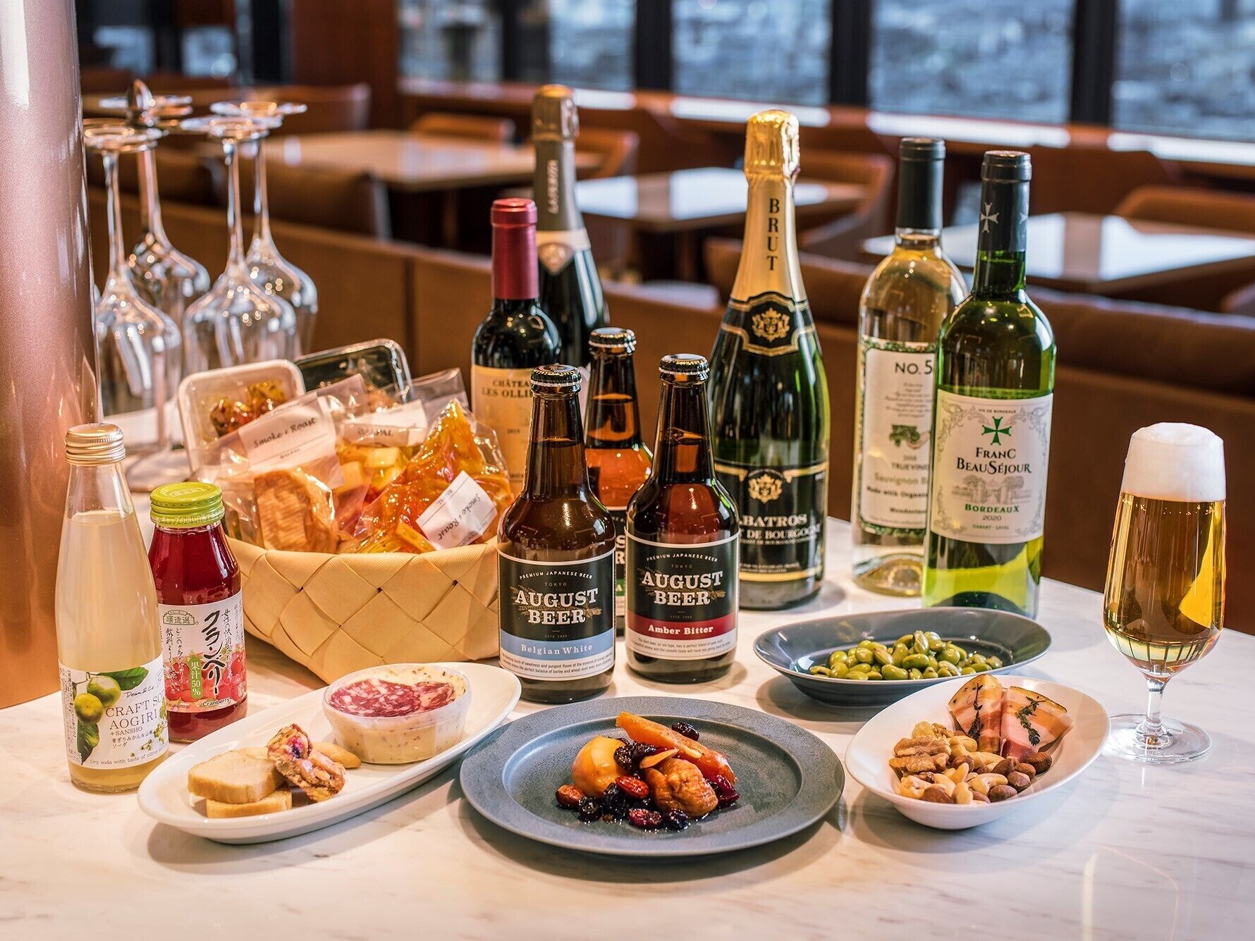 A table with various bottles of beer, wine, and a glass of white wine, accompanied by plates of food.