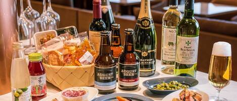 Una mesa con varias botellas de cerveza y vino, además de una copa de vino blanco, acompañada de platos de comida.