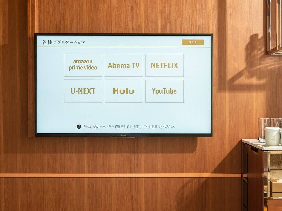 A wall-mounted TV displaying streaming services in Japanese.