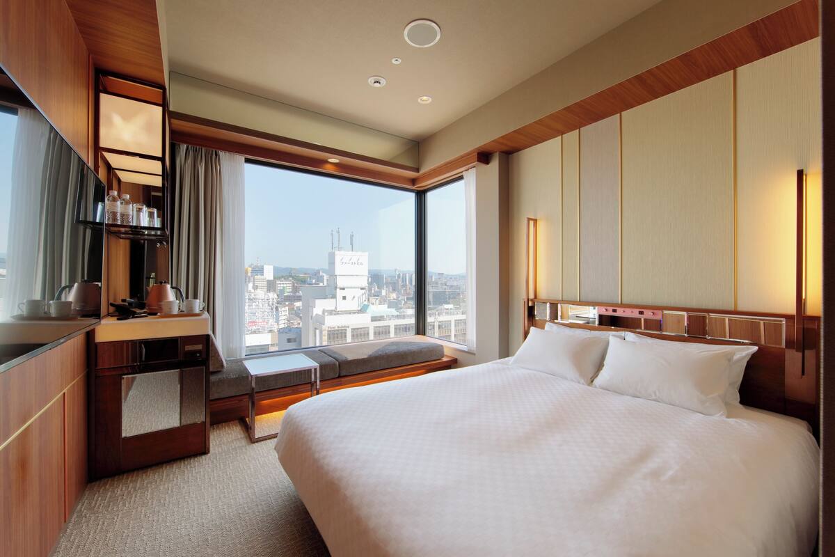 Habitación de hotel con una cama grande, zona de estar, escritorio y vistas a la ciudad.