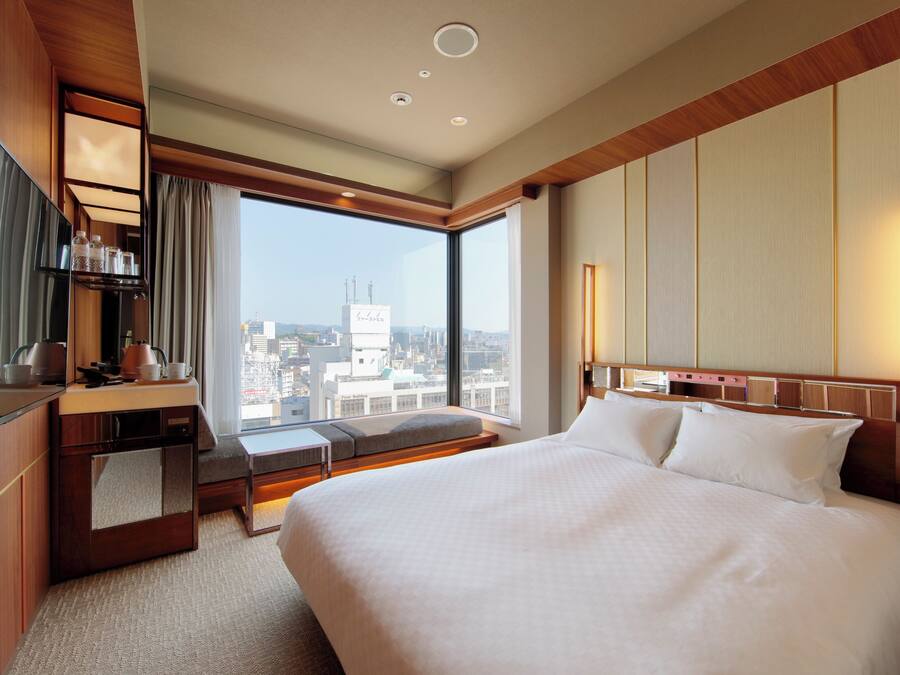 Une chambre d’hôtel dotée d’un grand lit, d’un coin salon, d’un bureau et offrant une vue sur la ville.