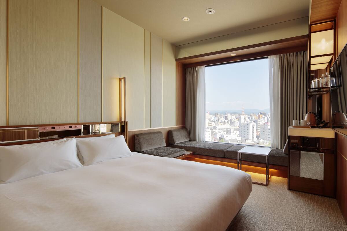 Una habitación de hotel con una cama grande, un sofá, un escritorio y vistas de la ciudad.
