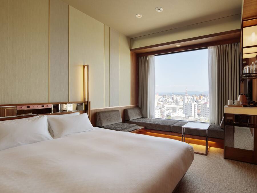 A hotel room with a large bed, a sofa, a desk, and a view of the city.