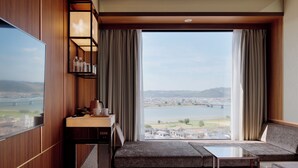 Una habitación de hotel con un ventanal grande, un sofá, una mesita y un televisor.