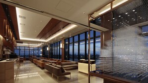 Un moderno vestíbulo de hotel con un amplio espacio de asientos, grandes ventanales que ofrecen vistas a la ciudad y una escultura de vidrio decorativa.