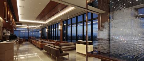 A modern hotel lobby with a spacious seating area, large windows offering city views, and a decorative glass sculpture.