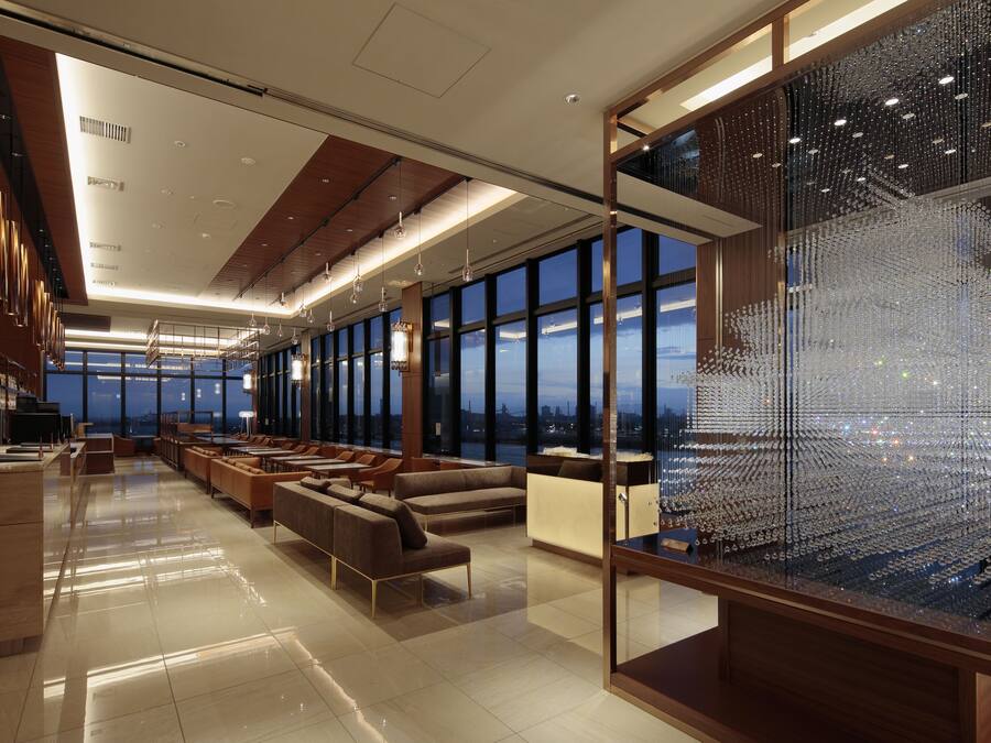 Een moderne hotelentree met een ruime zithoek, grote ramen met uitzicht op de stad, en een decoratieve glaskunstinstallatie.