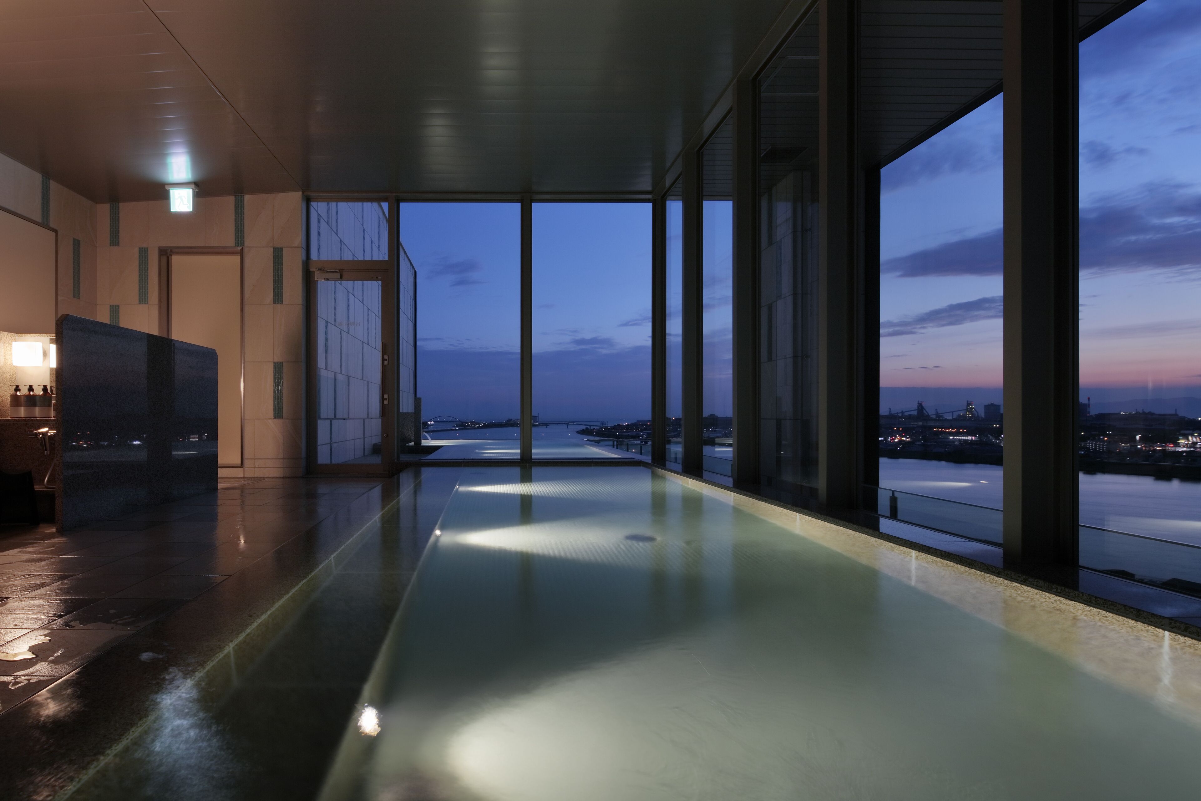 A modern indoor pool with a view of a cityscape at dusk.