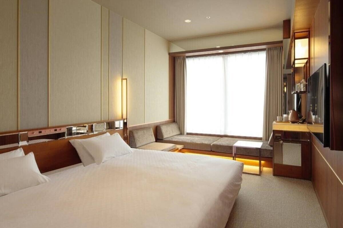 Habitación de hotel con una cama grande, zona de estar con vistas a la ciudad, televisor de pantalla plana y minibar.