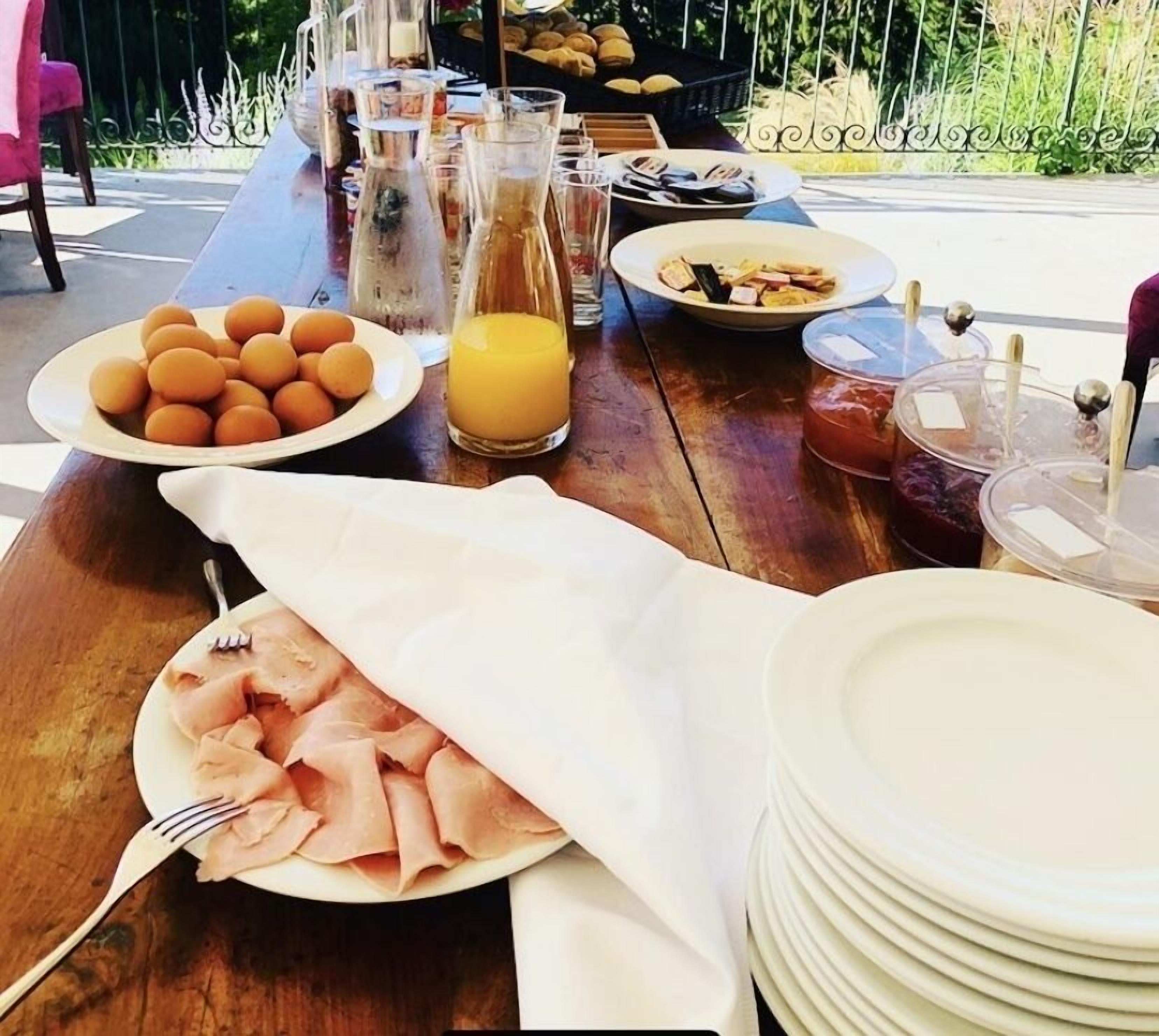 A breakfast table with plates of eggs, ham, and toast, a glass of orange juice, and a basket of bread.