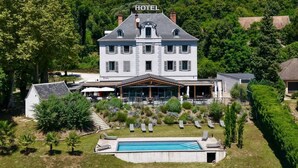 Un hotel grande con piscina, rodeado de vegetación exuberante y un jardín cuidado.