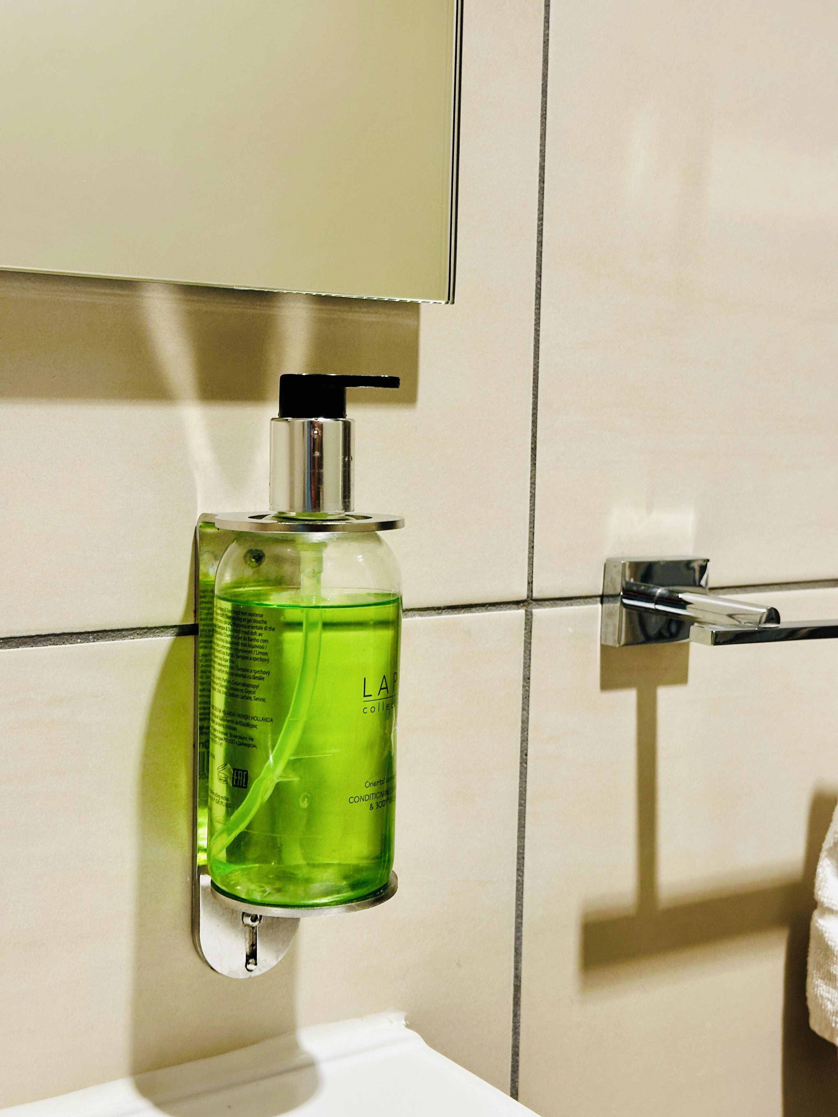 A bathroom with a green bottle of liquid soap mounted on a wall, a chrome faucet, and a mirror above.