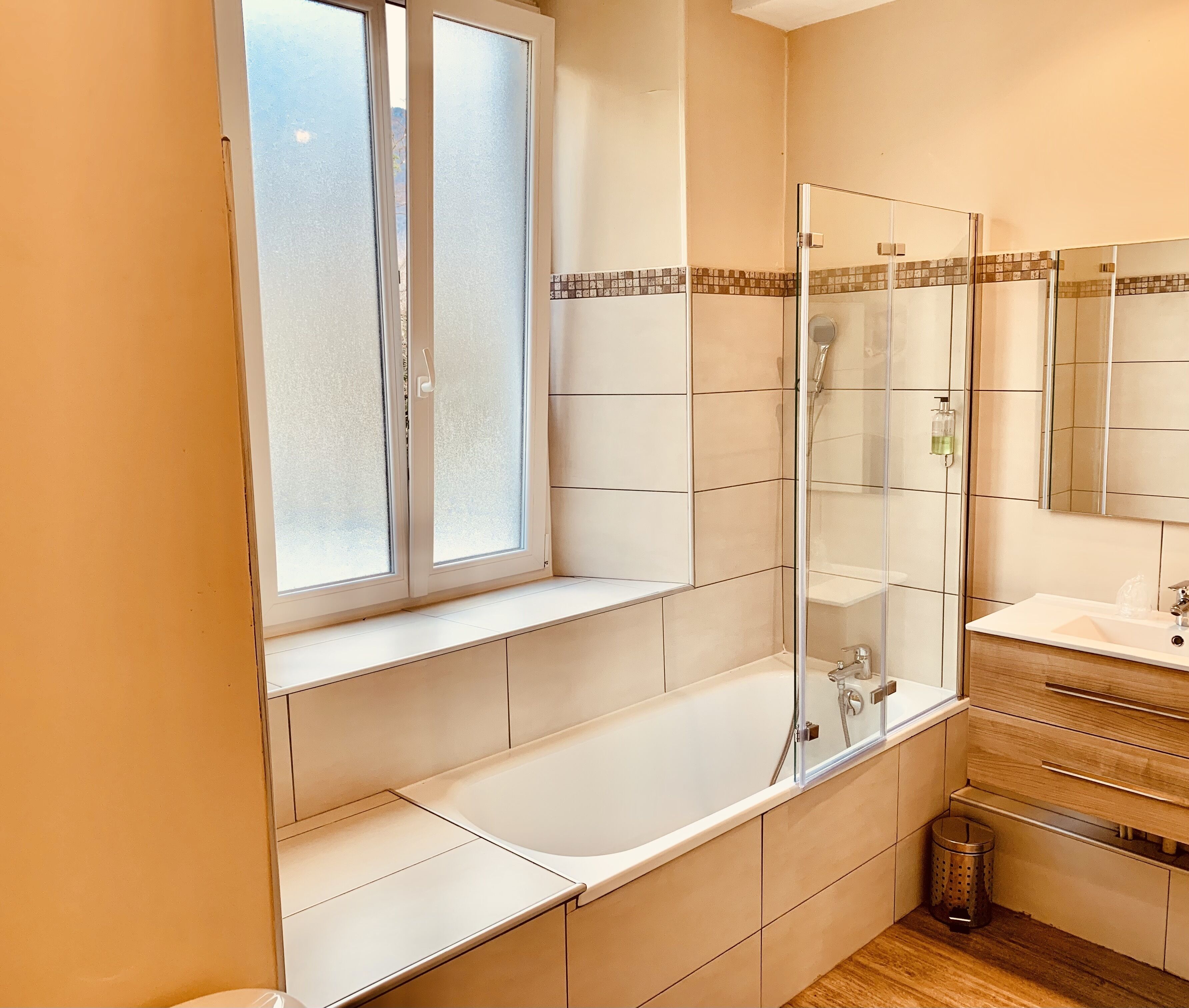 Un bagno moderno con cabina doccia in vetro, una vasca da bagno spaziosa, una finestra con vetro smerigliato e un mobile bagno in legno con specchio.