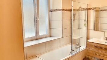 Un bagno moderno con cabina doccia in vetro, una vasca da bagno spaziosa, una finestra con vetro smerigliato e un mobile bagno in legno con specchio.