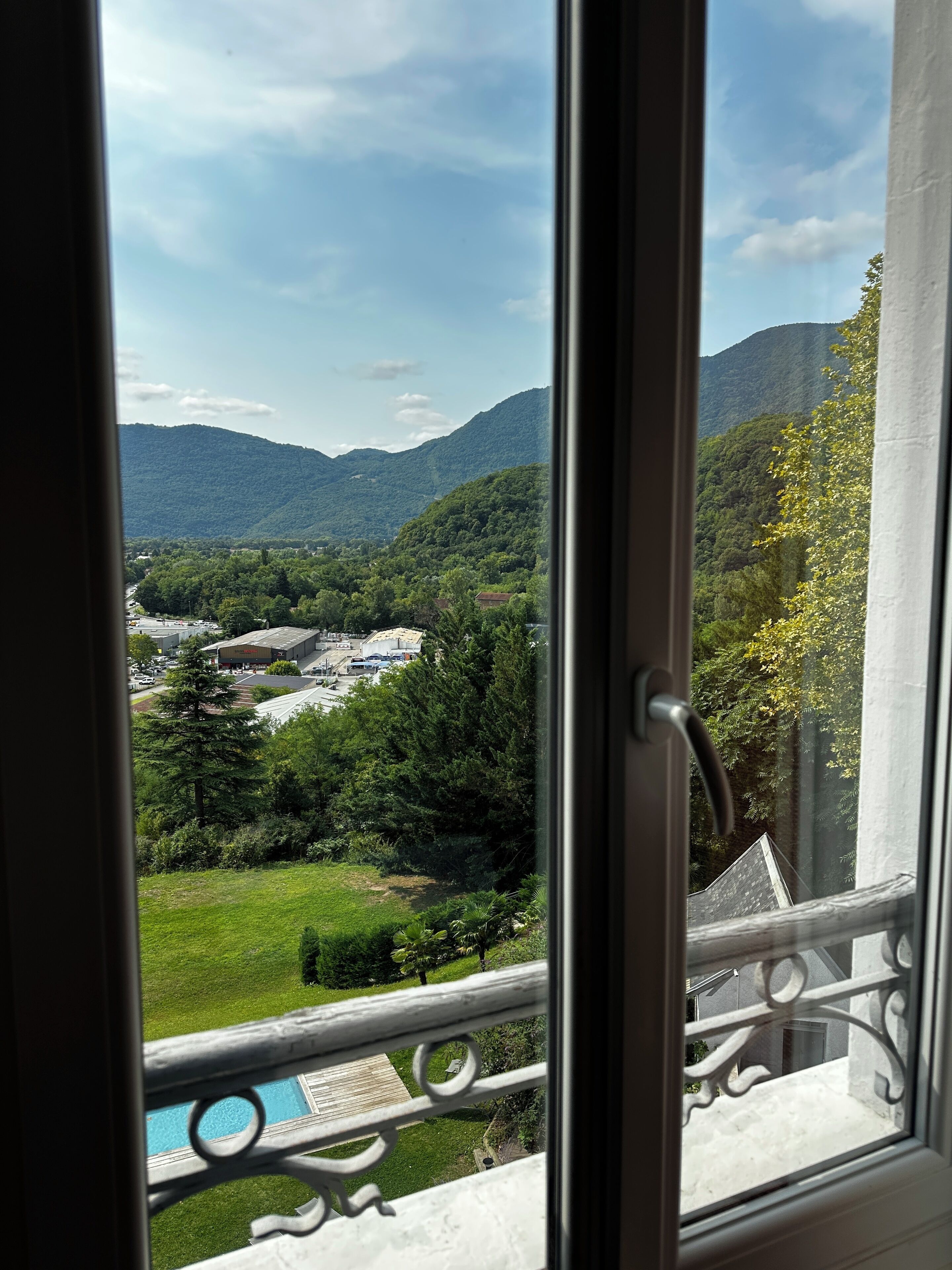 A view from a window overlooking a mountainous landscape with greenery and buildings.