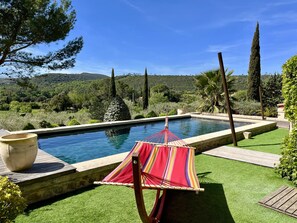 A pool with a hammock, green lawn, and a mountainous backdrop.