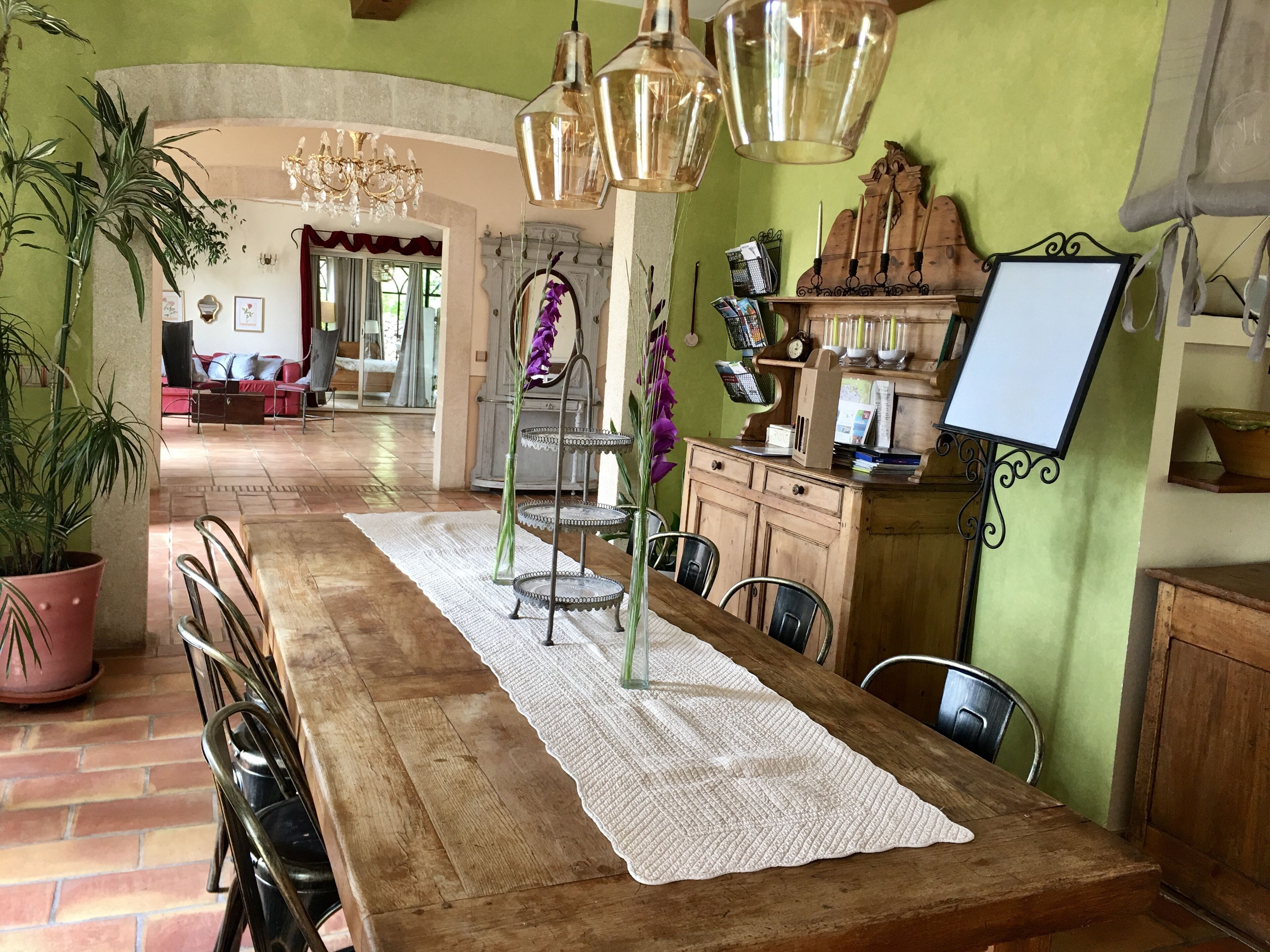 Un coin repas avec une table en bois, des chaises, un chemin de table blanc et un lustre.