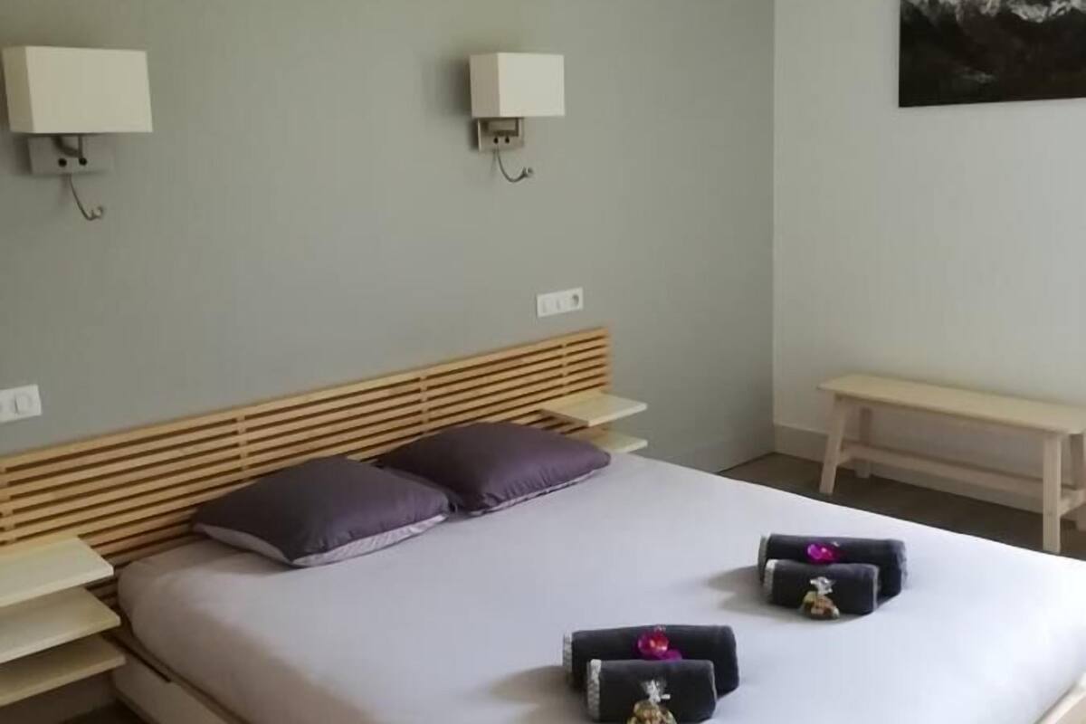 Una cama bien hecha con cabecera de madera, dos mesitas de noche y un pequeño banco.