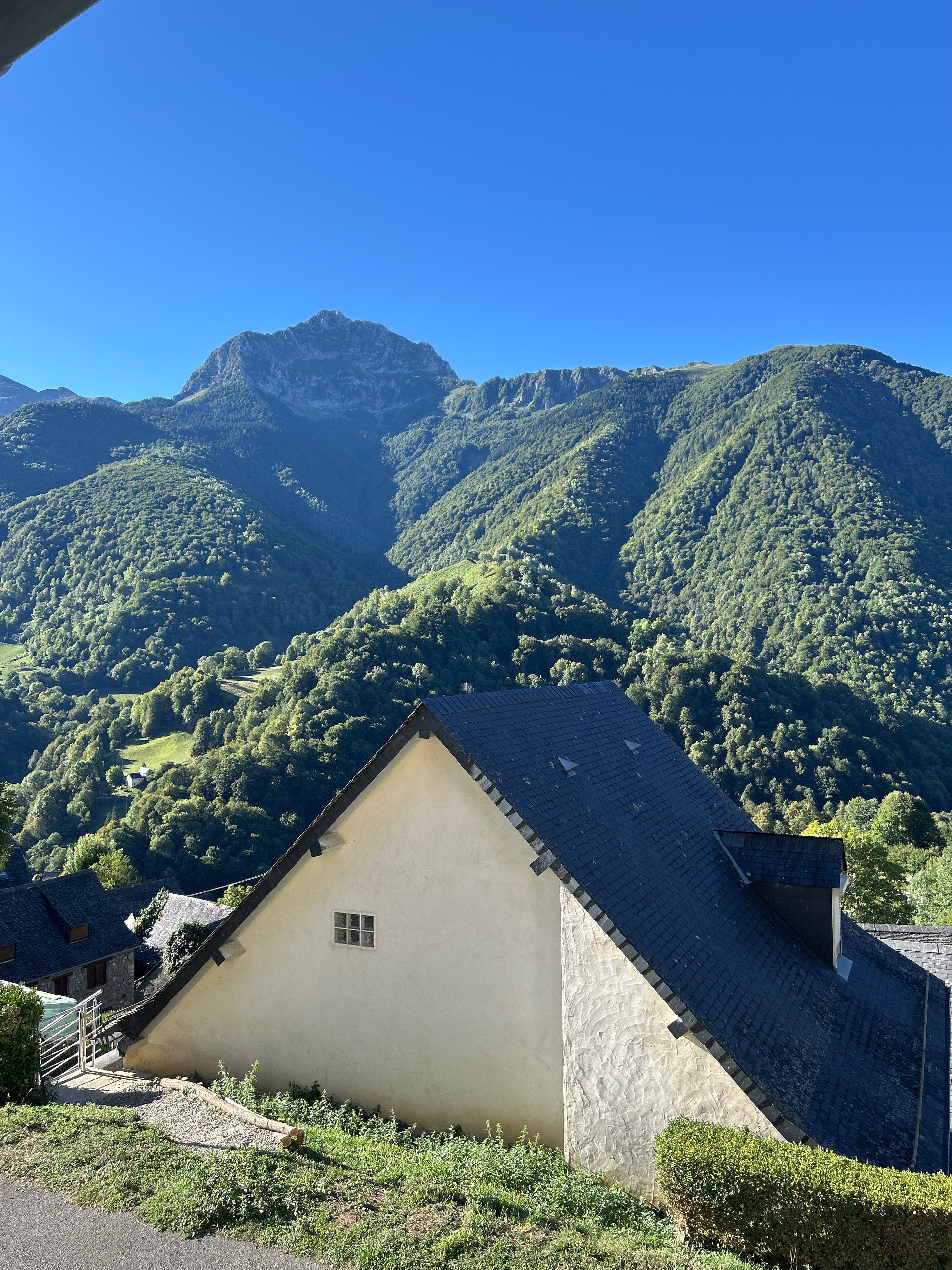 A building with a sloped roof, surrounded by lush green hills and a mountain in the background.
