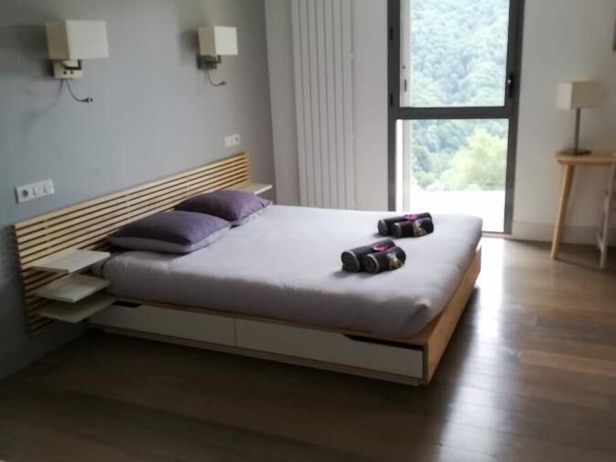 Un dormitorio moderno con una cama de madera, una ventana con vistas a zonas verdes y una mesita de noche con una lámpara.
