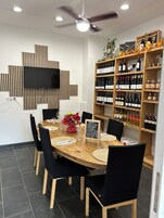 A dining area with a round table, black chairs, a television mounted on the wall, and a wine rack with various bottles.