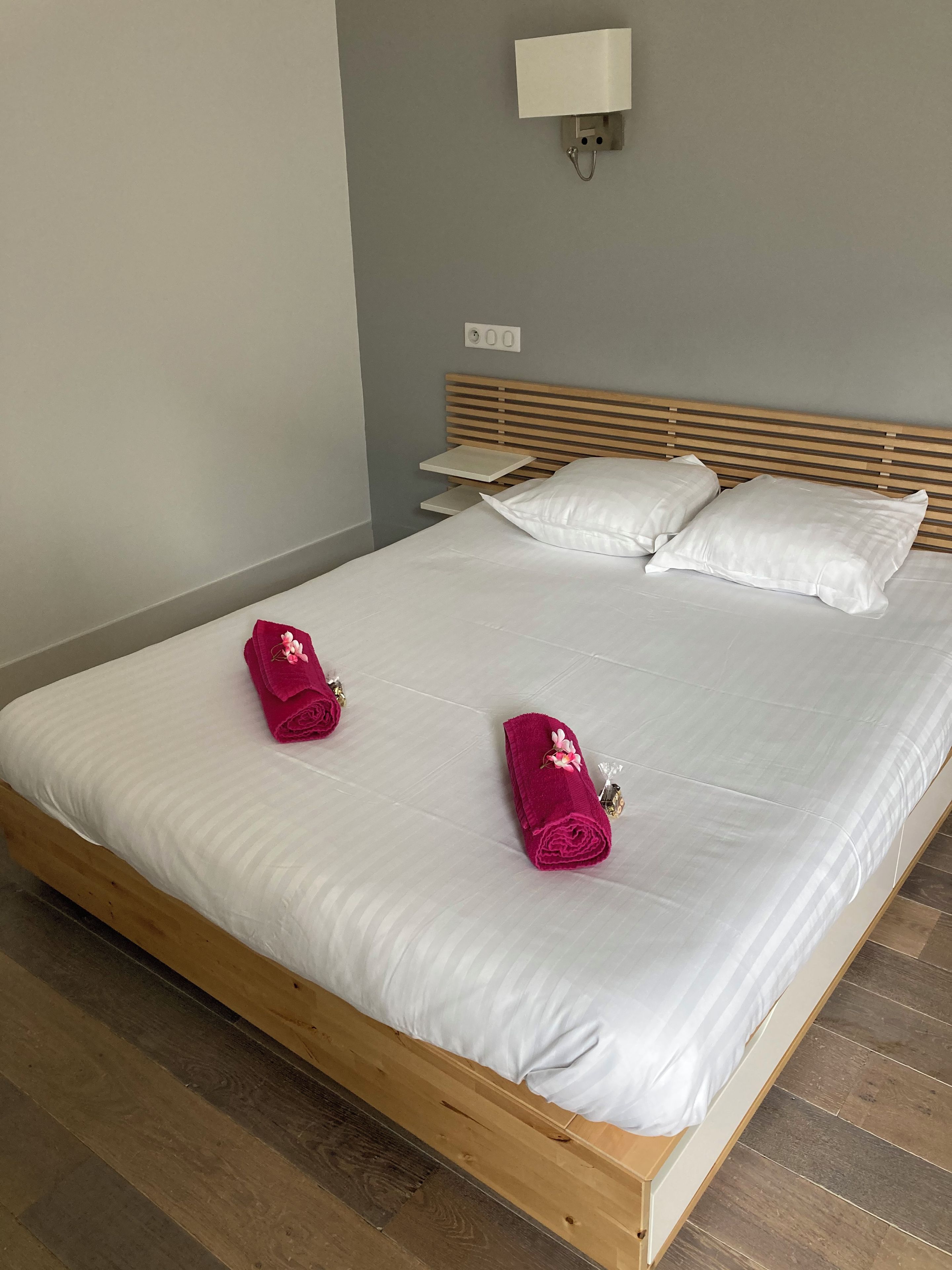 A neatly made bed with white sheets and two rolled towels on the bed.
