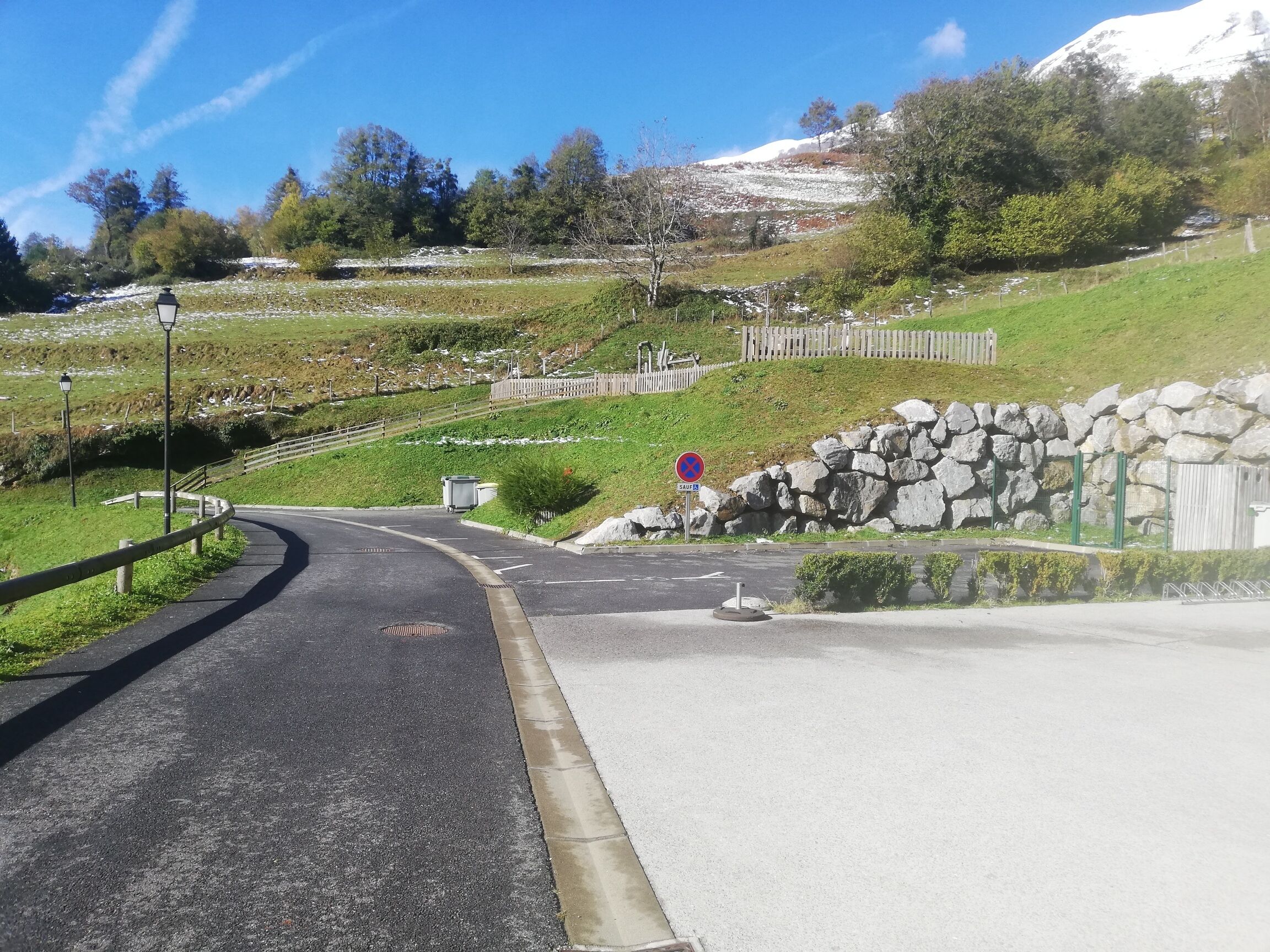 A winding road with a stone wall and a sign indicating a parking area.