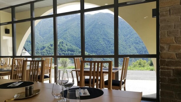 A dining area with tables set for two, large windows offering a view of a mountainous landscape. - Auberge des Isards (Aydius)
