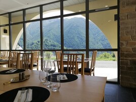 A dining area with tables set for two, large windows offering a view of a mountainous landscape.