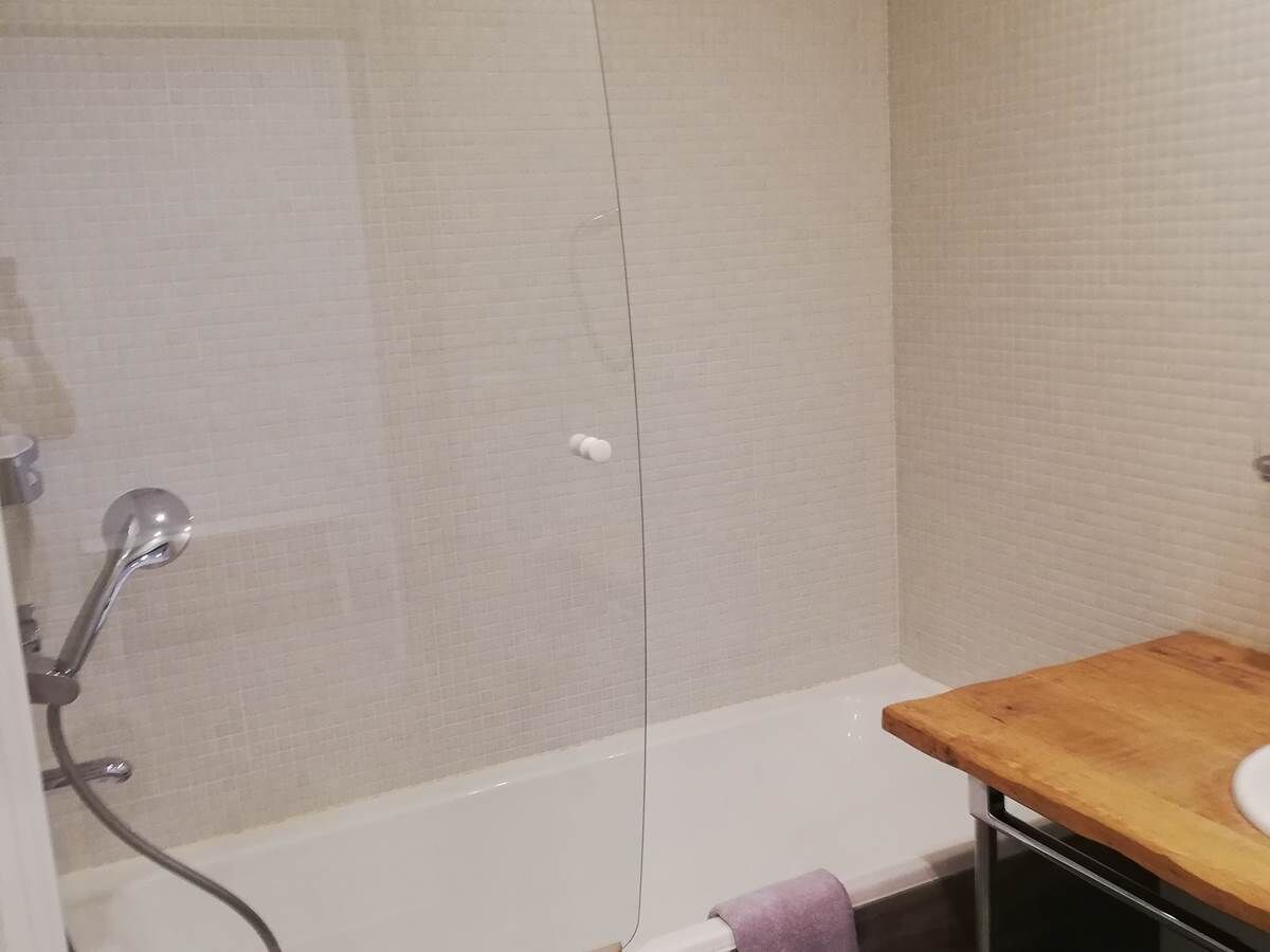 A bathroom with a shower, a wooden vanity, and a white bathtub.