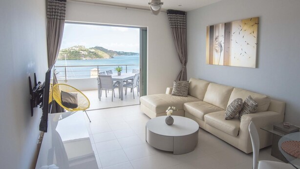 A modern living room with a sofa, coffee table, and a balcony with a view of the sea. - K & E Lemon Drop Cove (Cupecoy)