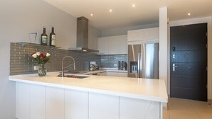 A modern kitchen with a central island, stainless steel appliances, and a black door in the background. - K & E Lemon Drop Cove (Cupecoy)