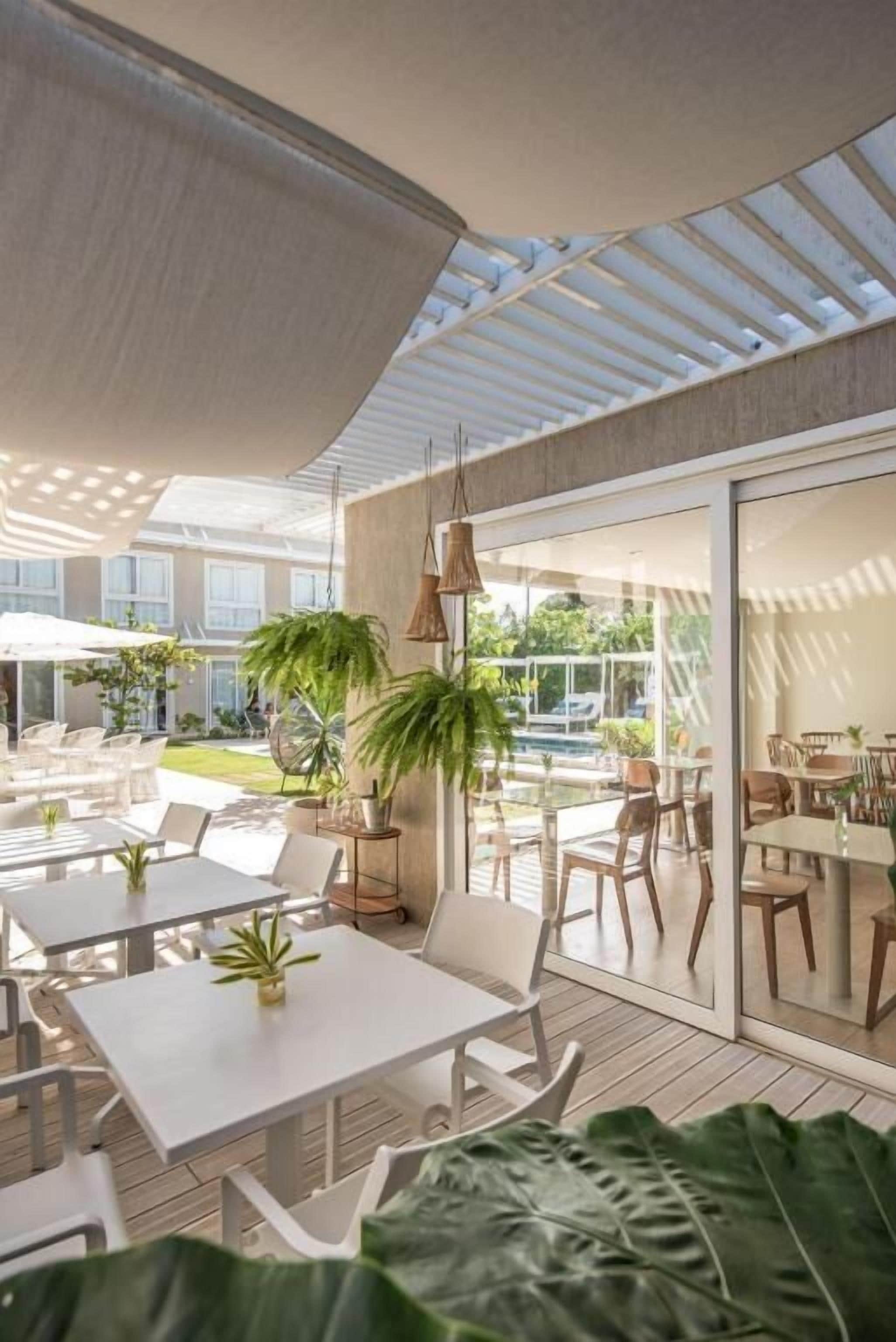 Un patio al aire libre con mesas y sillas, una sombrilla grande y plantas en macetas.